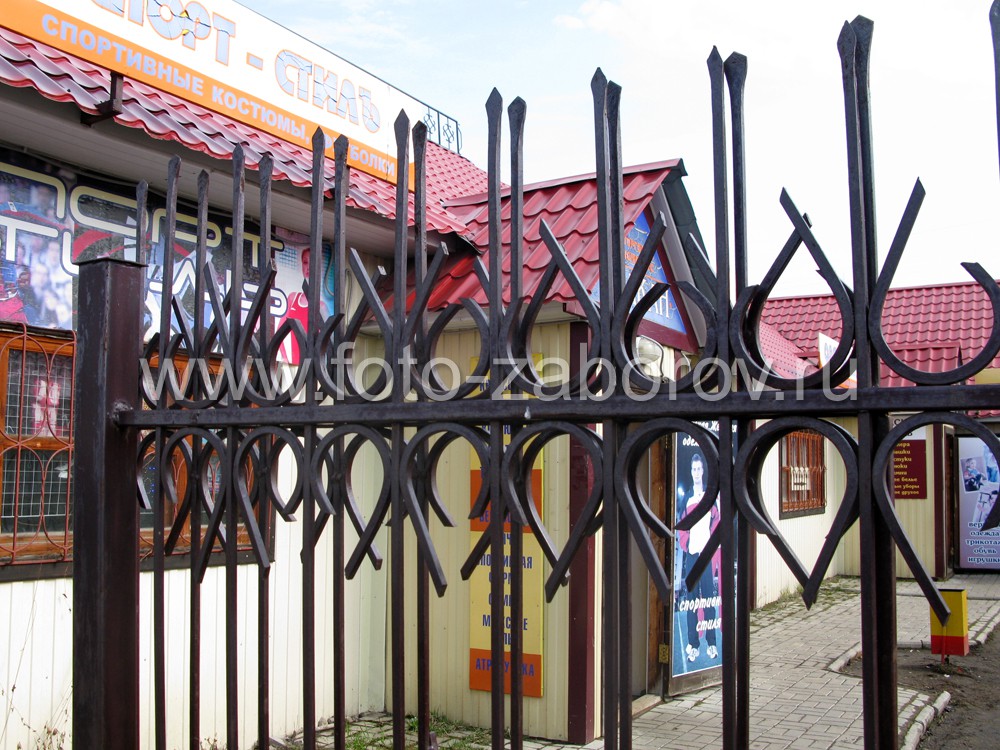 Фото Простенький металлический забор с декоративными эволютами ограждает торговые