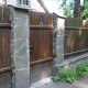 Деревянный забор тёмно-коричневого цвета с облицованными столбами под камень - основательность в каждом элементе.