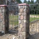 Ворота и калитка декорированы оригинальными коваными узорами, массивные столбы облицованы искусственным камнем.